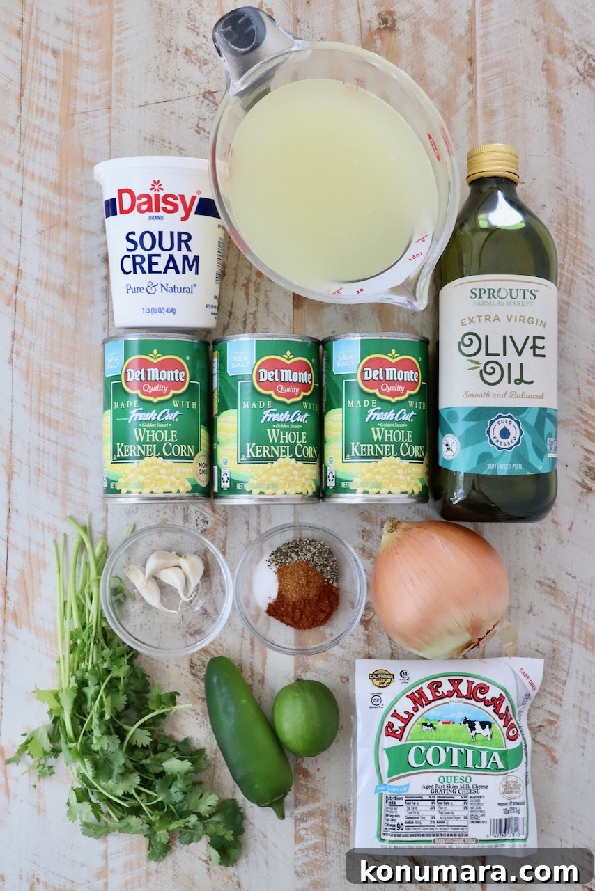 Mexican Street Corn Soup Recipe (Elote-Inspired) 3 A flat lay of Mexican street corn soup ingredients, including sour cream, canned corn, olive oil, spices, an onion, lime, jalapeño, cilantro, and cotija cheese on a wooden surface.