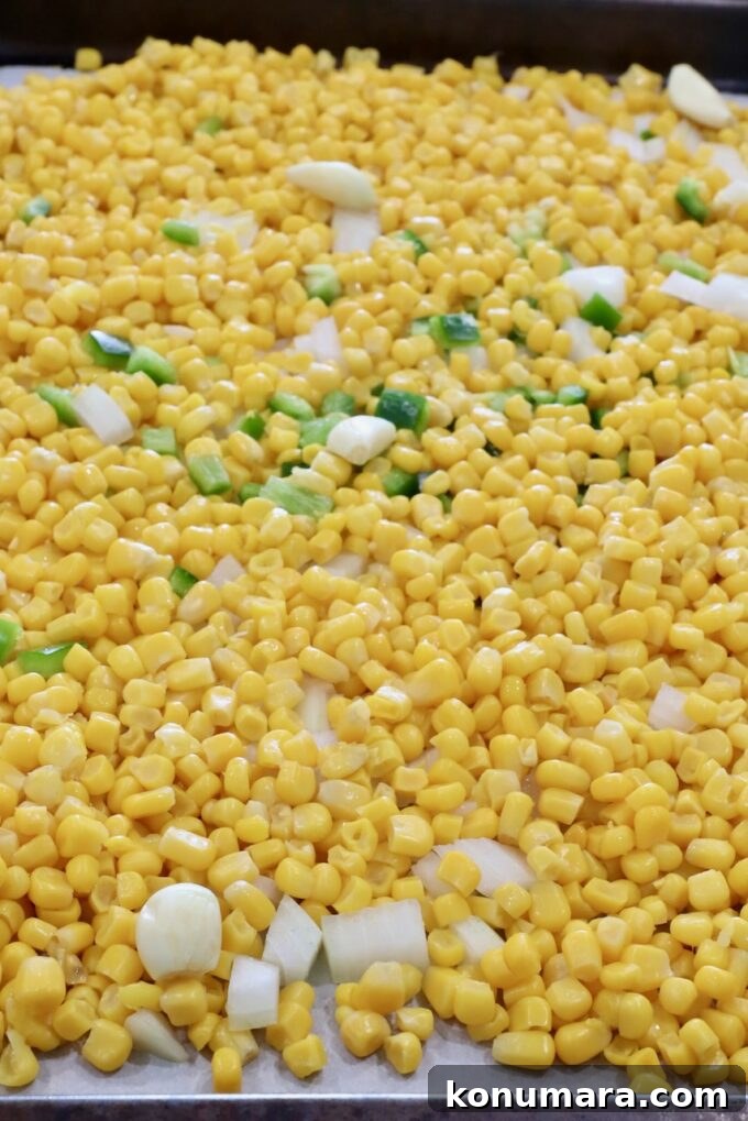 Mexican Street Corn Soup Recipe (Elote-Inspired) 4 kernels of corn mixed with diced onions, jalapenos and garlic cloves on a baking sheet