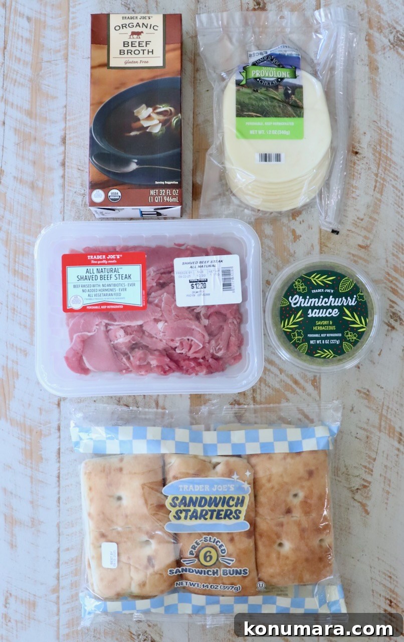 Various Trader Joe's products displayed on a wooden surface, including beef broth, provolone cheese, shaved beef steak, chimichurri sauce, and sandwich buns.