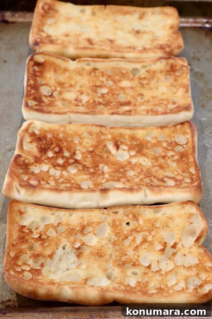 Golden-brown grilled sandwich bread slices on a baking tray, with a crispy, textured surface.