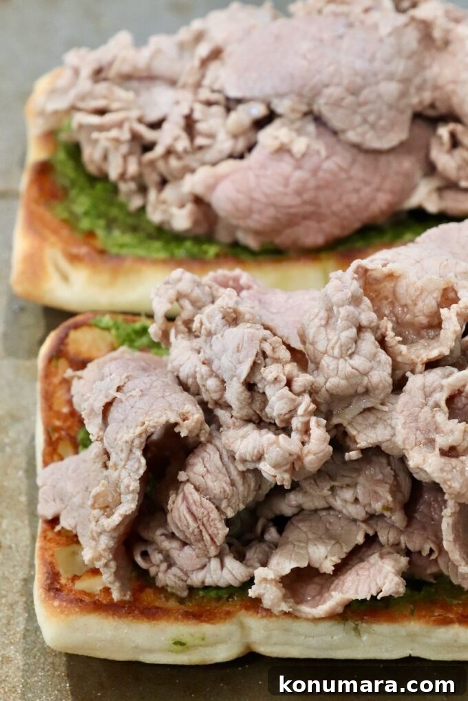 Close-up of two open-faced sandwiches with thinly sliced roast beef atop toasted bread with green chimichurri sauce