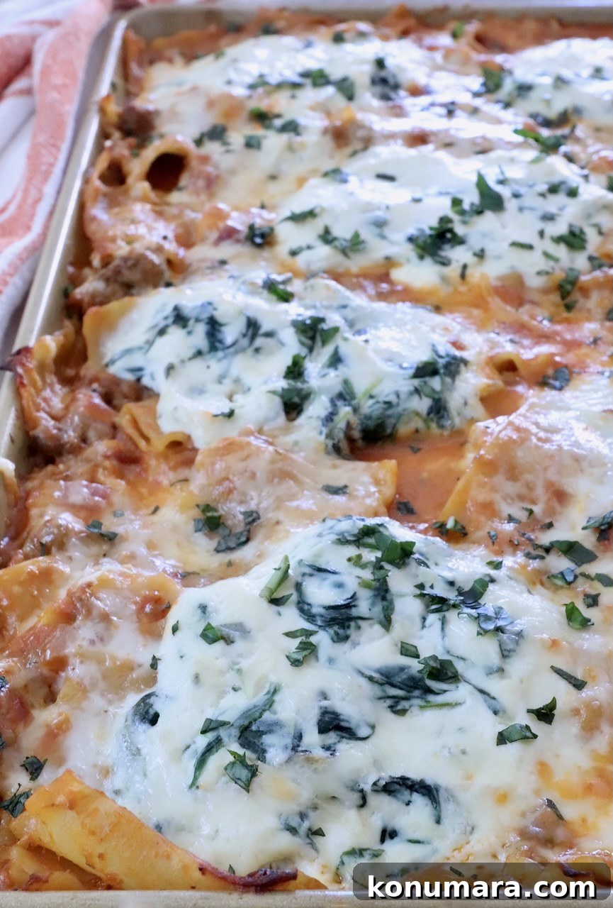 Sheet-Pan Butternut Squash Lasagna Recipe 10 Close-up of a baked pasta dish in a rectangular tray, topped with bubbling cheese and herbs.