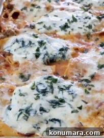 Close-up of a baked pasta dish in a rectangular tray, topped with bubbling cheese and herbs.