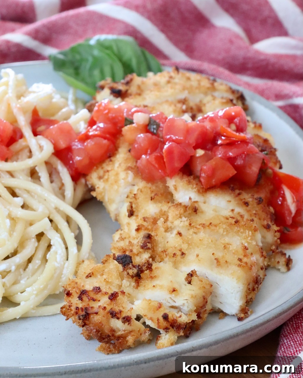Crispy Garlic Chicken Topped with Tomato Basil Bruschetta 2 sliced piece of crispy chicken on a plate with pasta, topped with tomato bruschetta