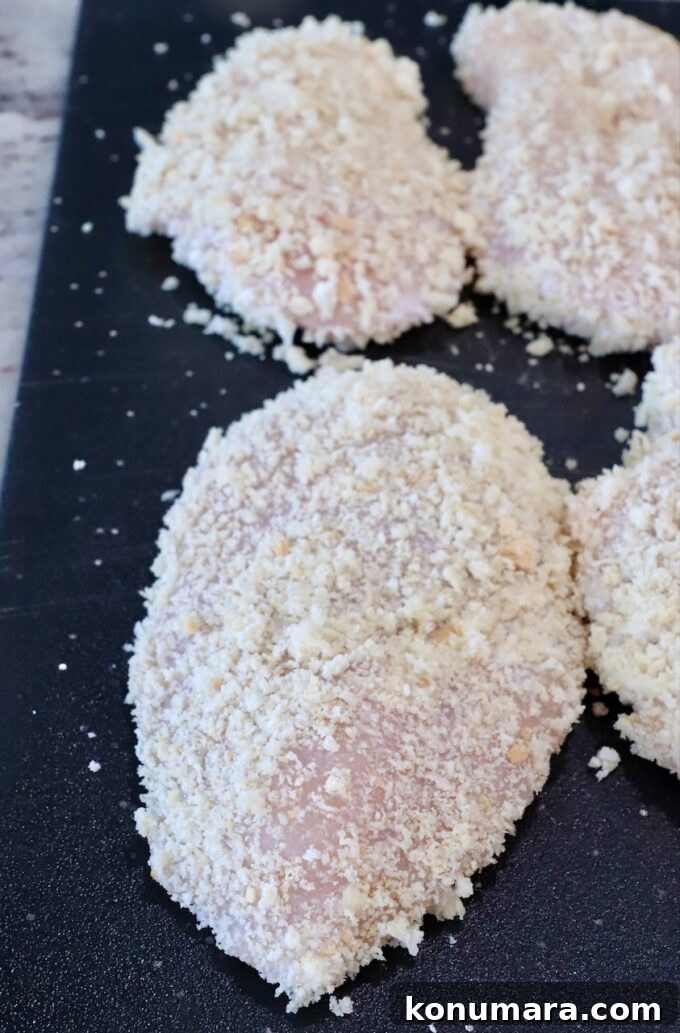 Crispy Garlic Chicken Topped with Tomato Basil Bruschetta 5 raw chicken breasts coated in breadcrumbs on a cutting board