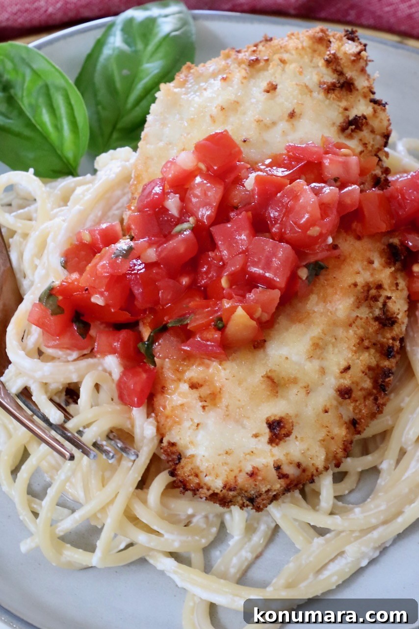 Crispy Garlic Chicken Topped with Tomato Basil Bruschetta 8 piece of crispy chicken on top of pasta on a plate, topped with tomato bruschetta, with basil leaves in the background