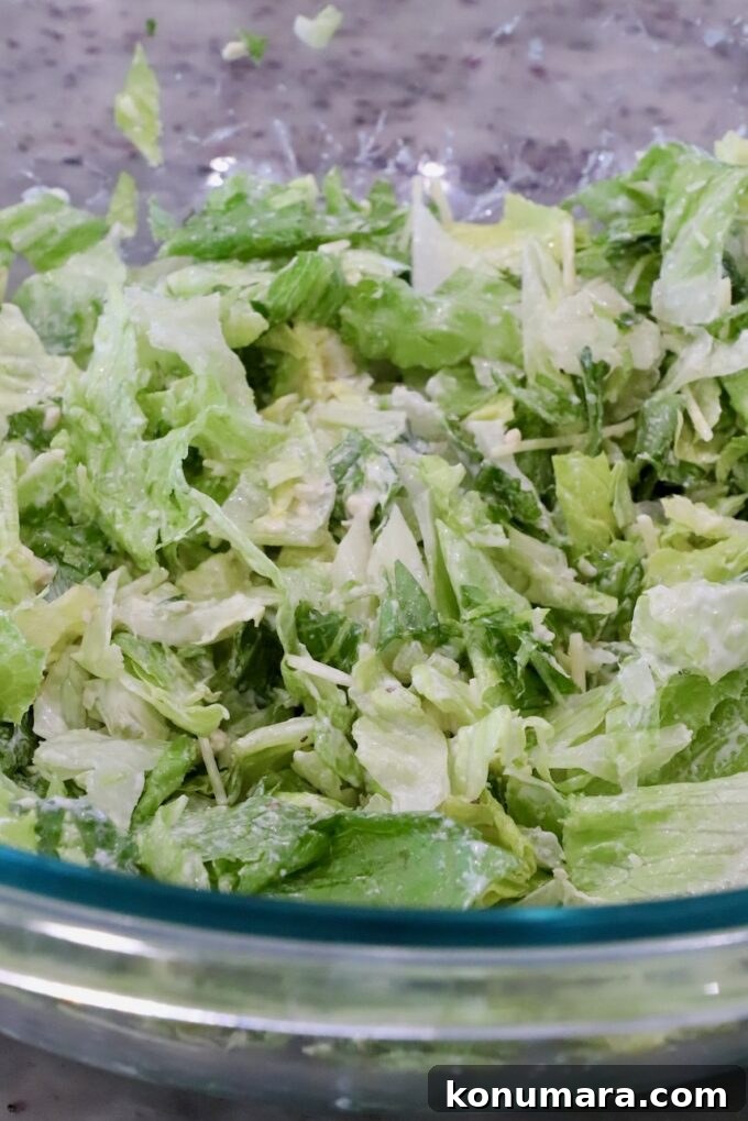 Chopped lettuce with grated cheese in a glass bowl on a speckled countertop.