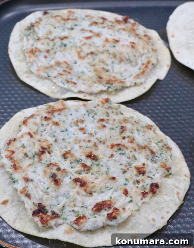 Two tortillas topped with an herb-speckled chicken mixture sit on a textured, dark griddle pan