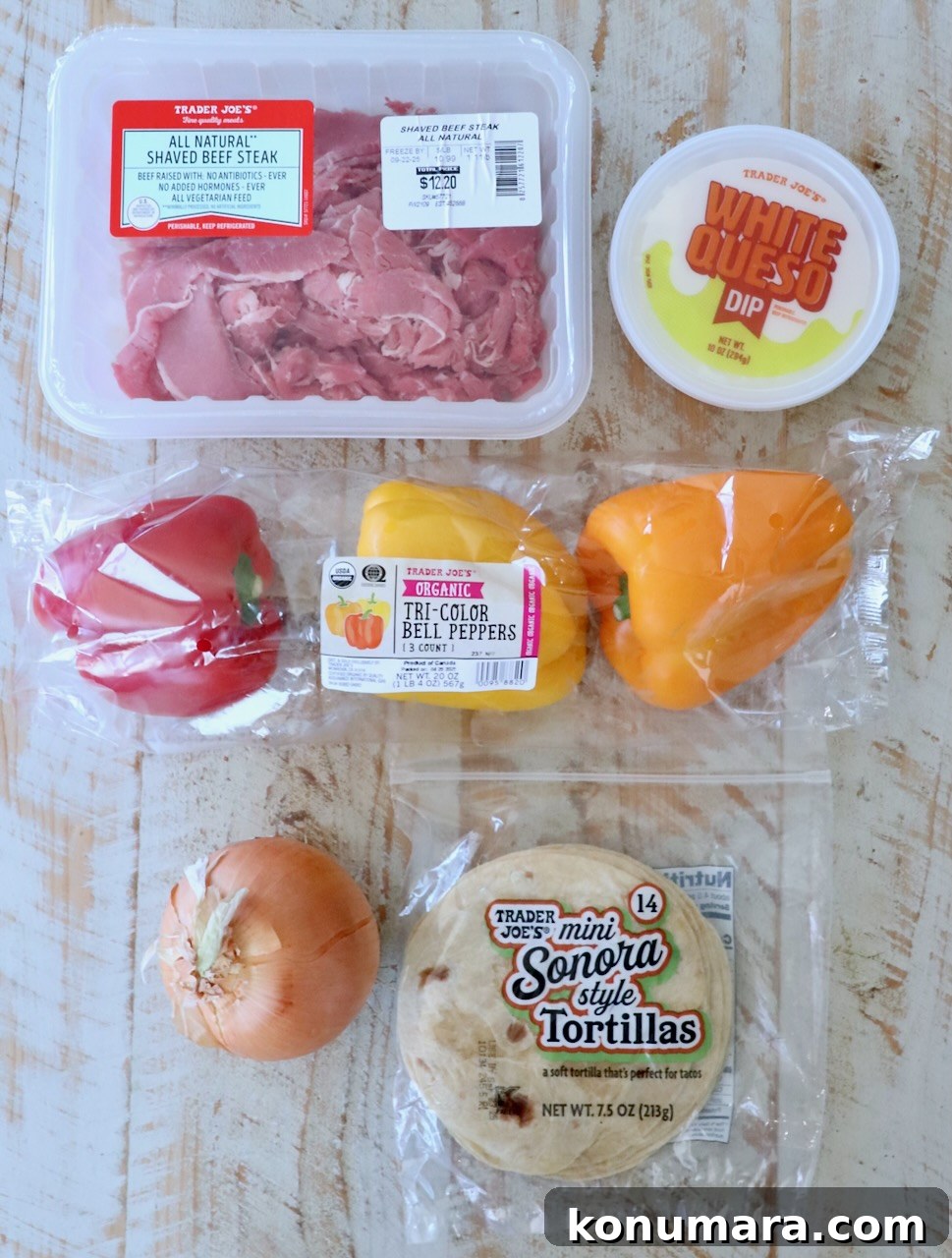 Assorted Trader Joe's ingredients on a wooden surface: shaved beef steak, white queso dip, tri-color bell peppers, a yellow onion, and mini tortillas.