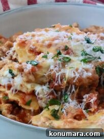 Close-up of a bowl of baked ravioli with melted cheese, garnished with fresh herbs with a fork in the bowl. Behind it, a red-striped cloth.