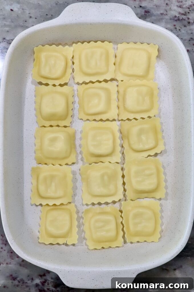 White baking dish with 15 uncooked ravioli in neat rows on a marble countertop.