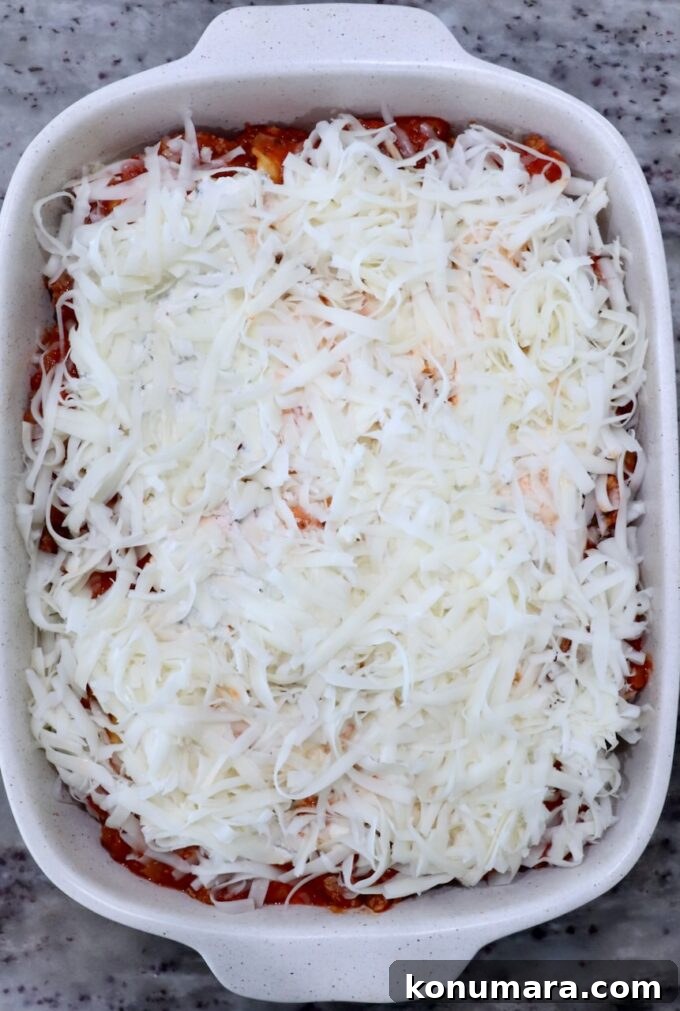A casserole dish filled with baked ravioli, topped generously with shredded cheese. The cheese covers a layer of tomato sauce.
