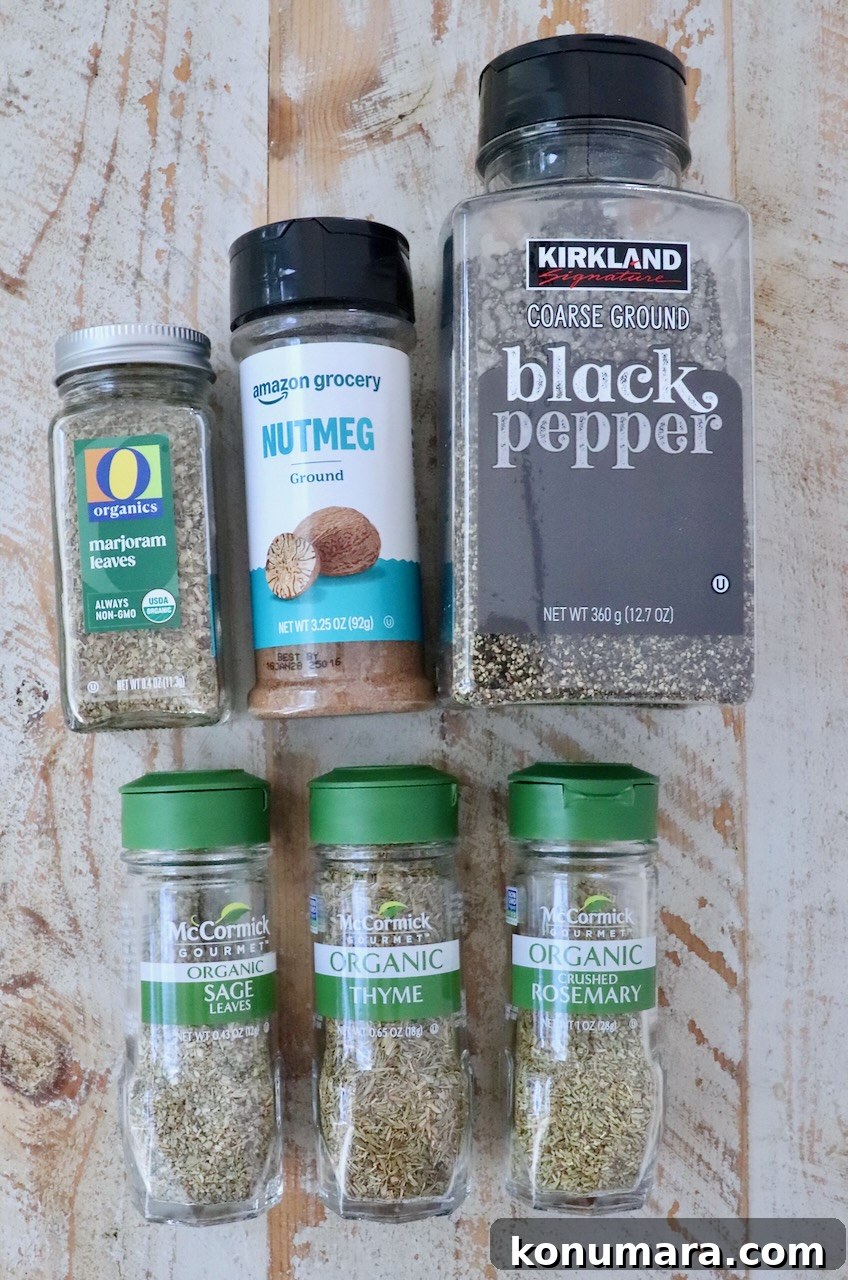 How to Make Poultry Seasoning at Home 3 A collection of six spice bottles on a wooden surface, including black pepper, nutmeg, marjoram, sage, thyme, and rosemary, all in clear containers.