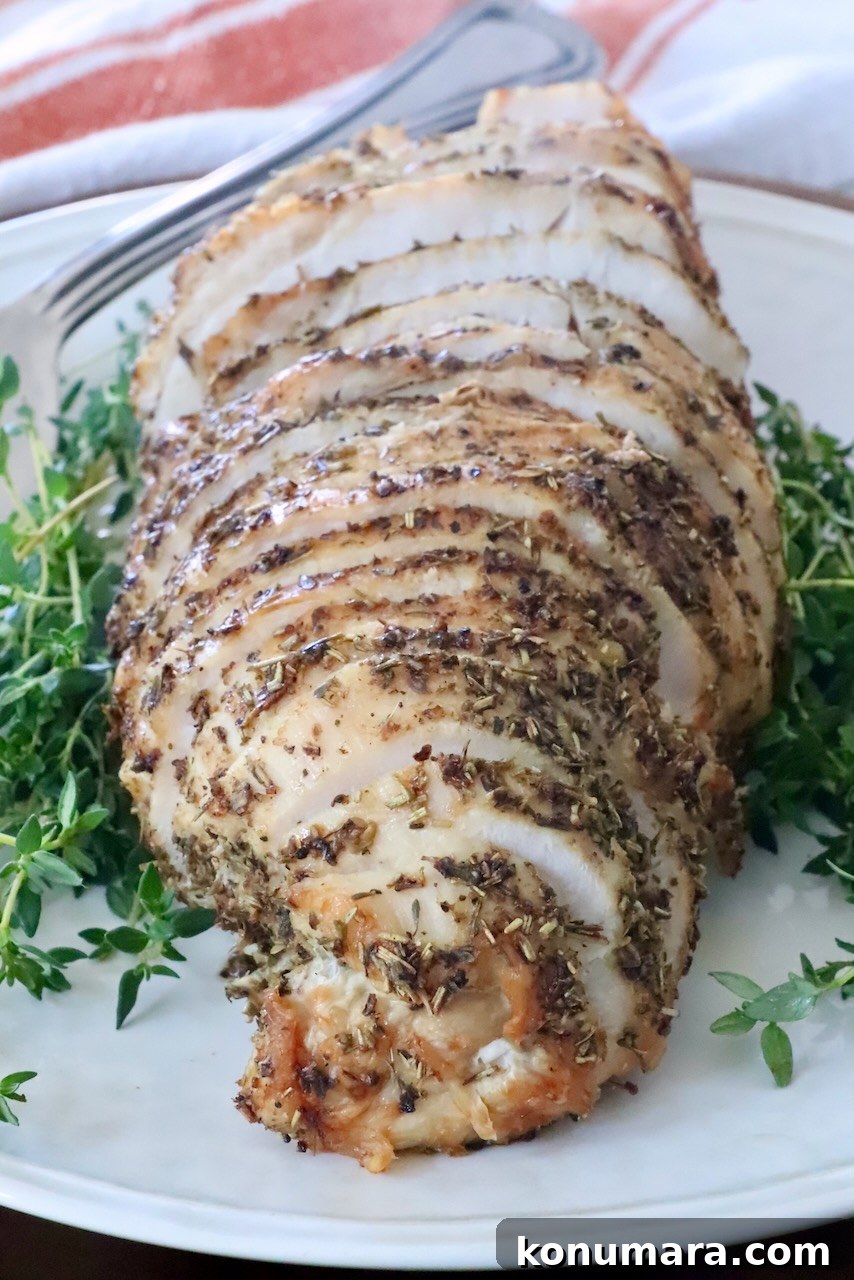 How to Make Poultry Seasoning at Home 4 Sliced herb-crusted roast turkey breast on a white plate, surrounded by fresh green herbs.