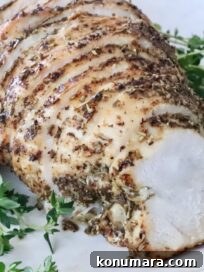 Sliced herb-crusted cooked turkey breast on a white plate, surrounded by fresh green herbs.