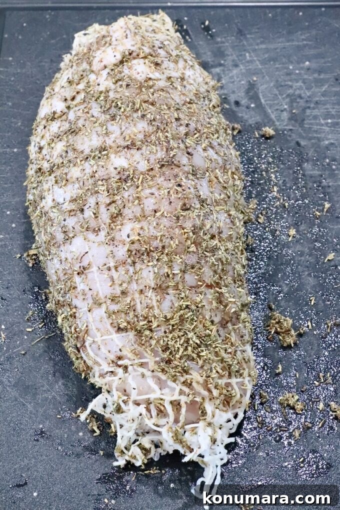 Turkey breast roast wrapped in netting, covered in an herb rub on a black cutting board