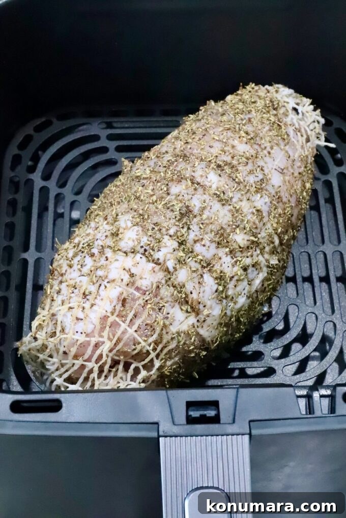 Turkey breast roast wrapped in netting, covered in an herb rub in an air fryer basket