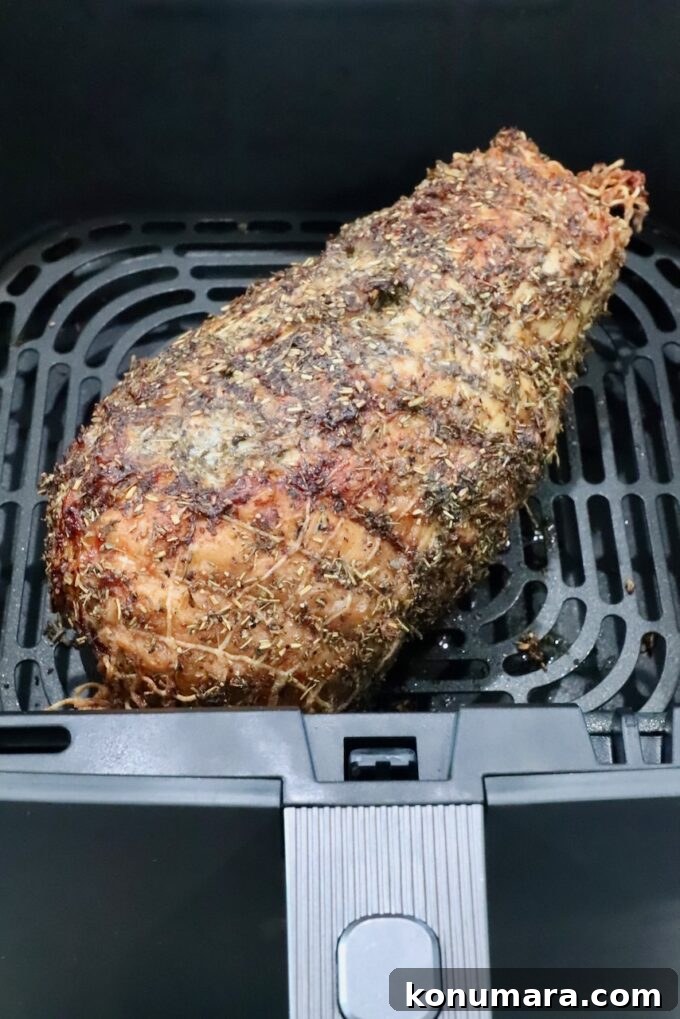 Cooked turkey breast roast wrapped in netting, covered in an herb rub in an air fryer basket