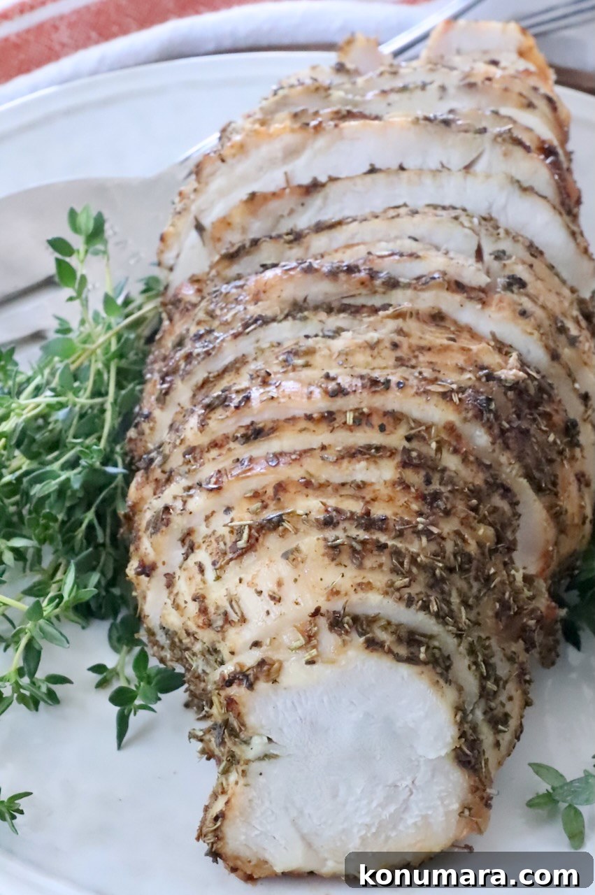 Sliced herb-crusted roast turkey breast on a white plate, surrounded by fresh green herbs.