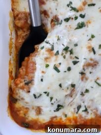 Close-up of butternut squash baked ravioli in a white dish. It features a golden-brown cheese topping sprinkled with herbs, with a serving spatula on the side.