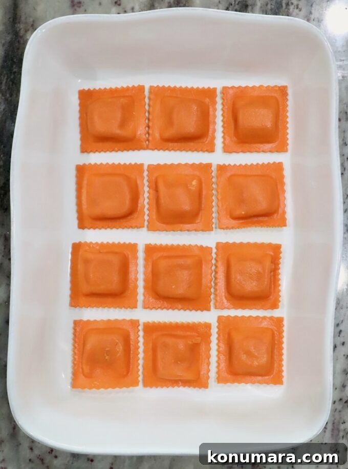 Baked Butternut Squash Ravioli with Brown Butter and Sage 6 Twelve pumpkin ravioli arranged neatly in a rectangular white dish on a marble countertop