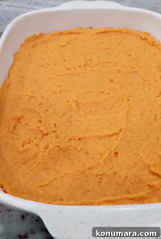 Creamy orange mashed potatoes in a white square dish, spread evenly.