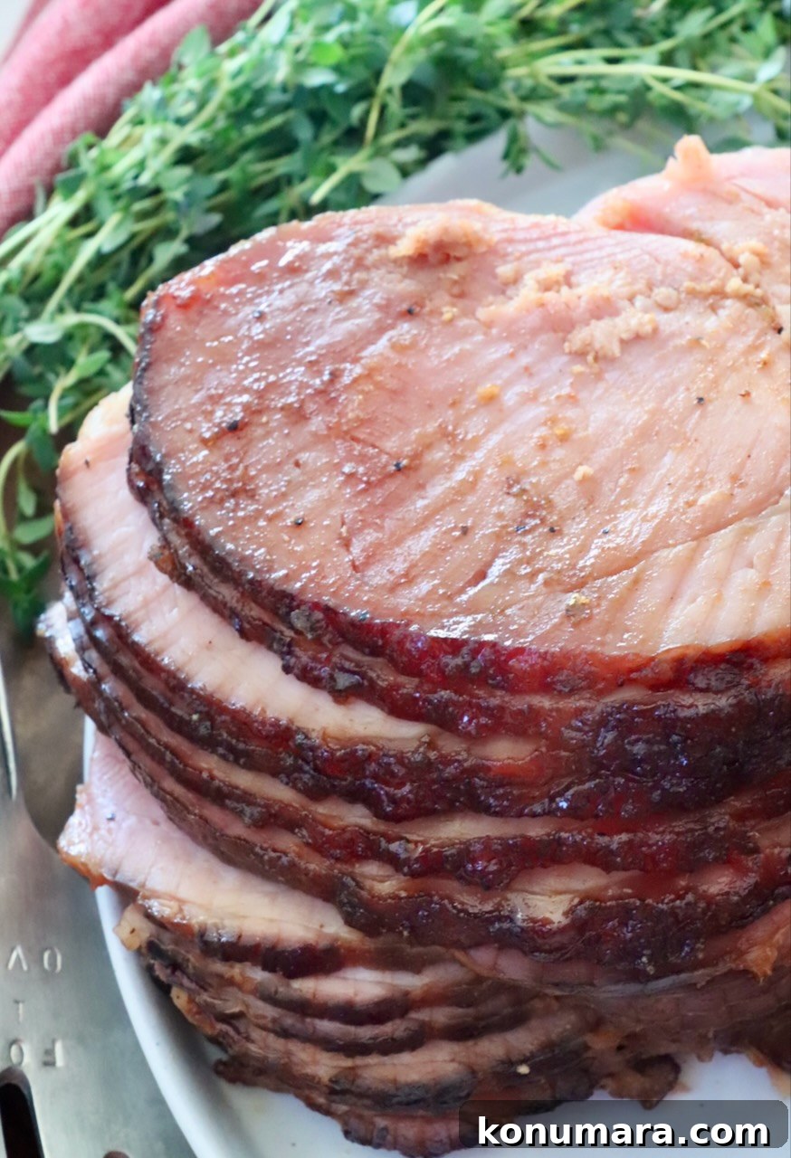 How to Smoke a Ham: Glaze, Time, and Temperature 13 Close-up of a glazed, spiral-cut ham on a white platter, showcasing juicy, tender slices. Fresh herbs and a red cloth are pictured in the background.