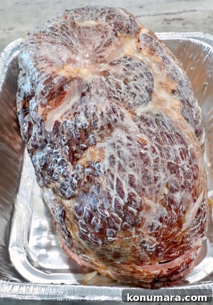 How to Smoke a Ham: Glaze, Time, and Temperature 4 Cooked ham covered with melted butter, placed in a shiny aluminum tray.