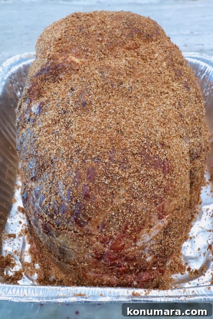How to Smoke a Ham: Glaze, Time, and Temperature 5 A large, seasoned ham covered in a brown sugar spice rub sits in an aluminum pan on a gray countertop, ready for cooking.