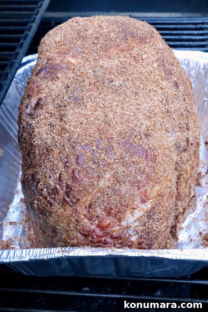 How to Smoke a Ham: Glaze, Time, and Temperature 6 A seasoned ham covered in a brown sugar spice rub rests in a foil tray on a smoker.
