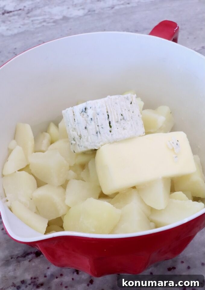 cubed potatoes in a red bowl with a stick of butter and a round of herbed cheese on top