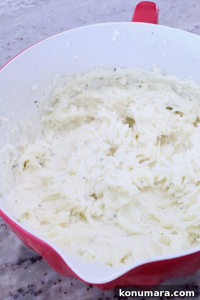 Mashed potatoes in a red and white bowl on a speckled countertop. The texture appears creamy and smooth