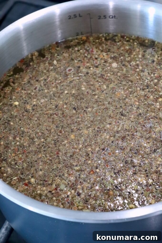 A silver pot filled with a simmering mixture of seeds and spices in liquid
