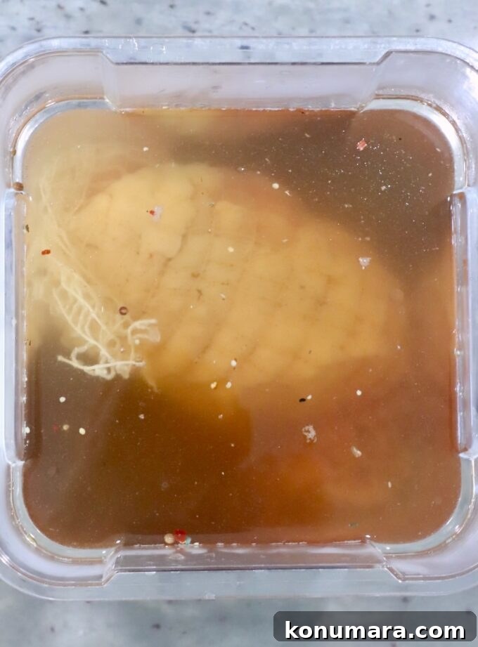 A turkey breast is submerged in a light brown brine within a plastic container.