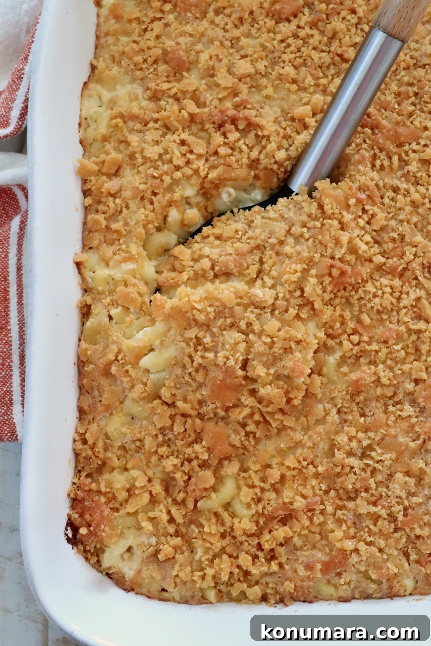Golden-brown baked macaroni and cheese with a crispy cracker topping in a white casserole dish. A serving spoon is lifting a portion, revealing creamy pasta underneath.