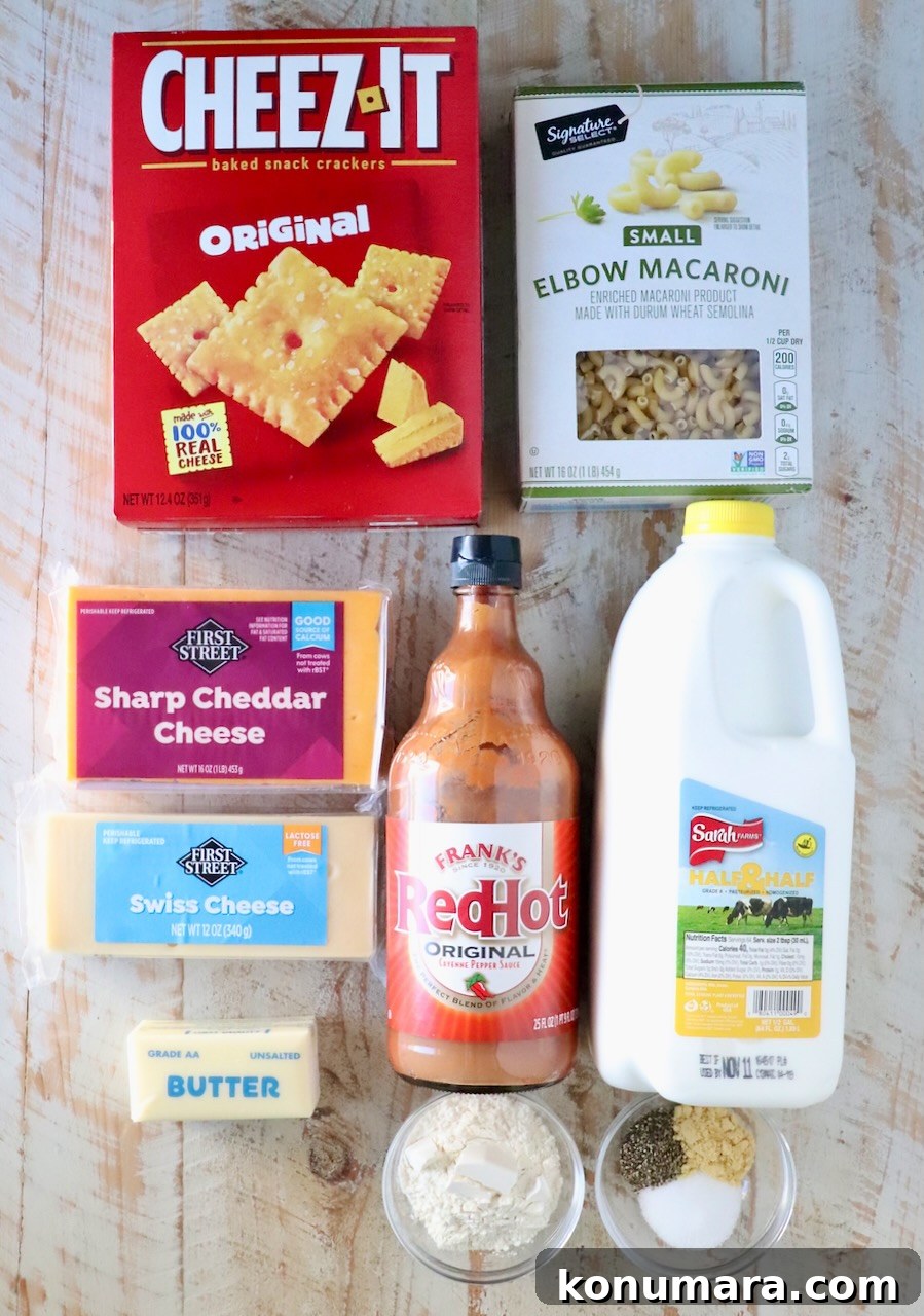 Assorted ingredients for mac and cheese on a wooden surface, including a box of Cheez-It crackers, elbow macaroni, cheddar and Swiss cheeses, hot sauce, milk, butter, flour, and spices.
