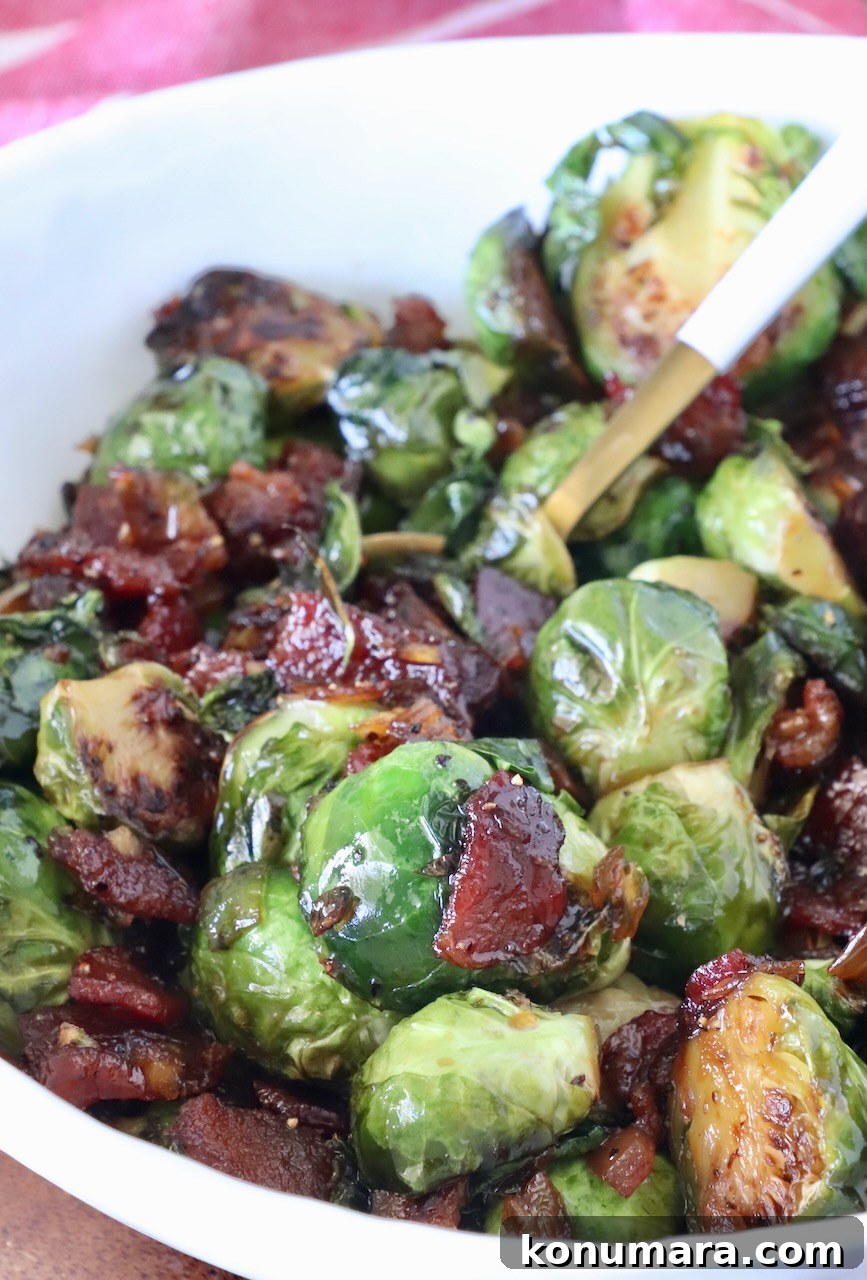 Caramelized Brussels sprouts with crispy bacon pieces in a white bowl. The sprouts are glazed, showing a glossy texture.