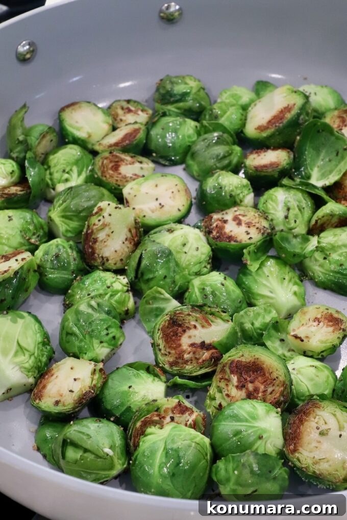 Brussels sprouts are halved and being sautéed in a pan. Their vibrant green color contrasts with golden-brown sear marks.