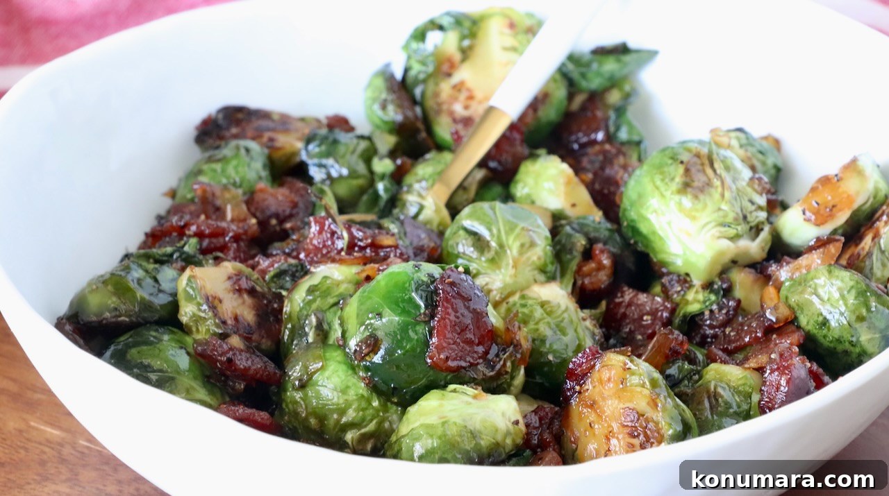 A white bowl filled with caramelized Brussels sprouts mixed with crispy bacon pieces, glistening with glaze, and a spoon for serving.