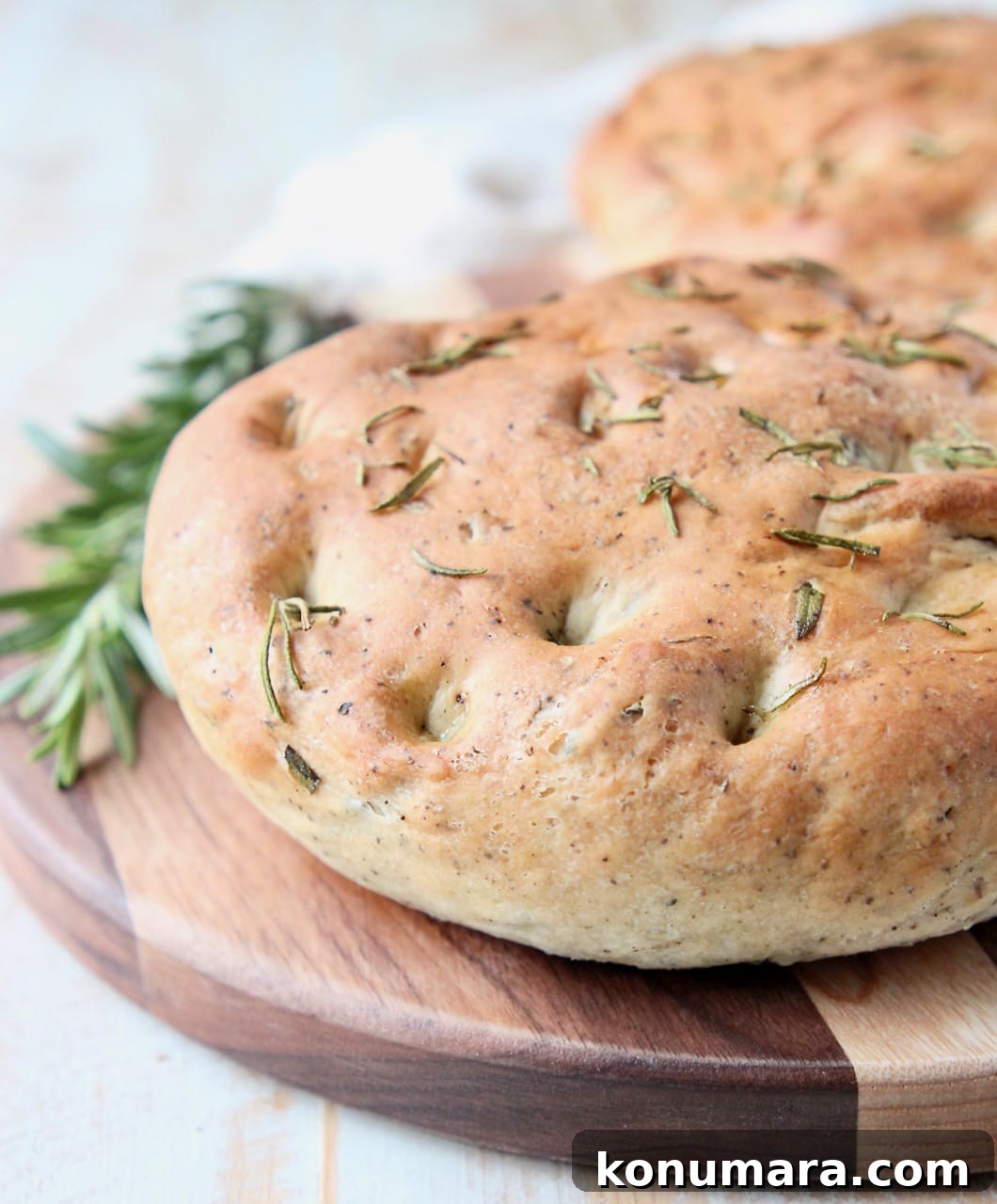 Rosemary focaccia bread on wood cutting board with fresh rosemary sprigs