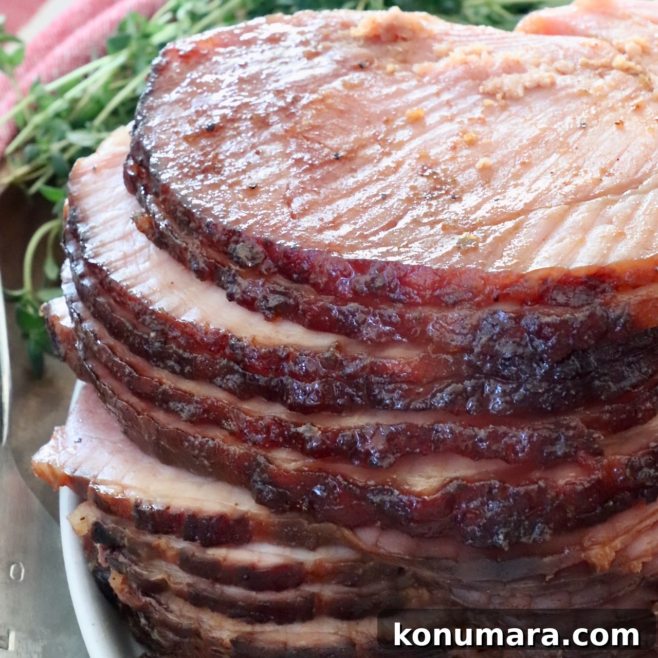 Sliced spiral ham glazed to a shiny brown, stacked on a white plate.
