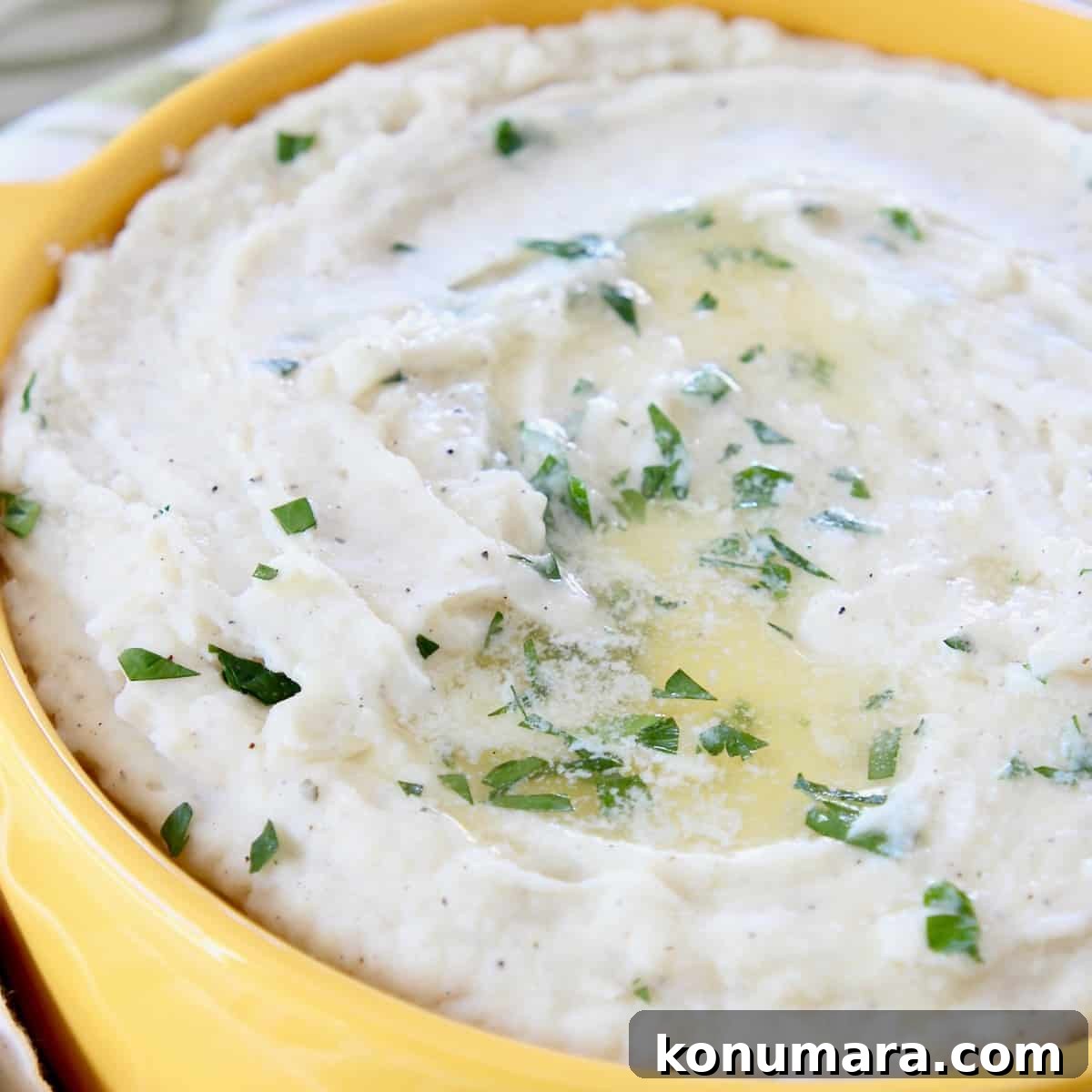 mashed potatoes topped with melted butter and chopped parsley in yellow bowl
