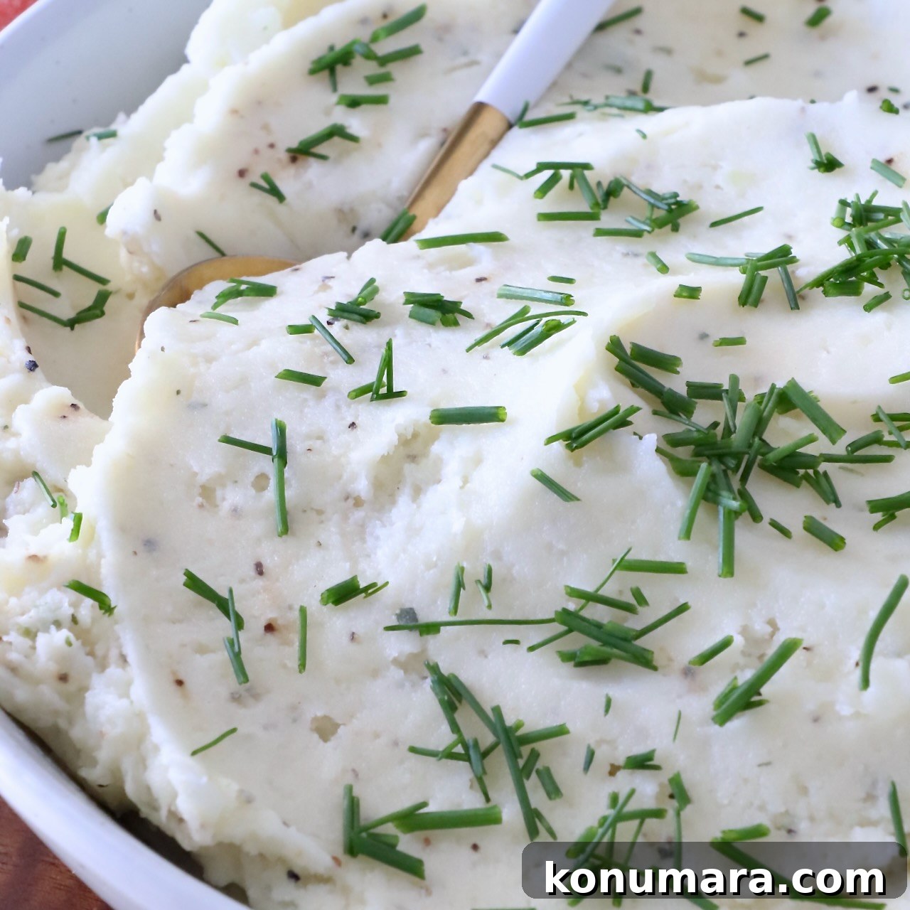 Creamy mashed potatoes garnished with fresh chopped chives in a white bowl.