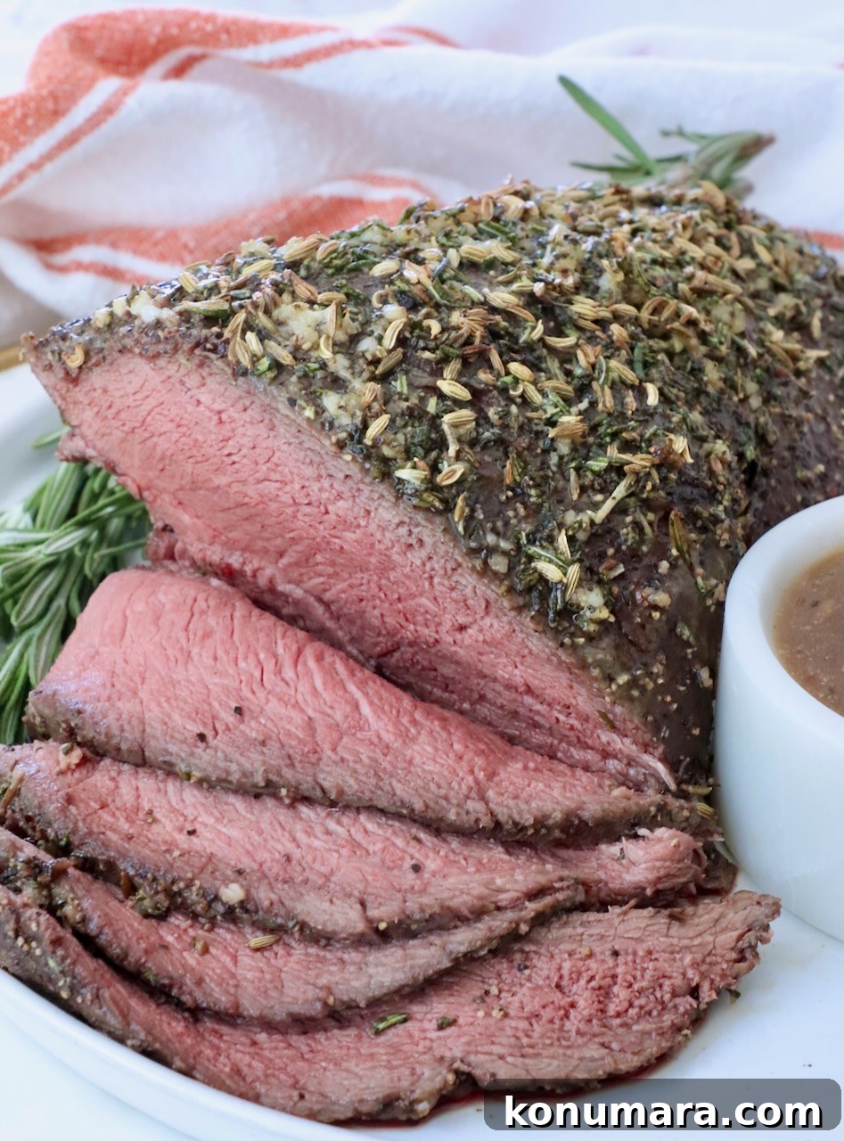 Sirloin Tip Roast Recipe for Tender, Juicy Results 2 Roast beef topped with herbs and spices, sliced to reveal a juicy pink interior. Garnished with rosemary and served on a white plate with gravy.