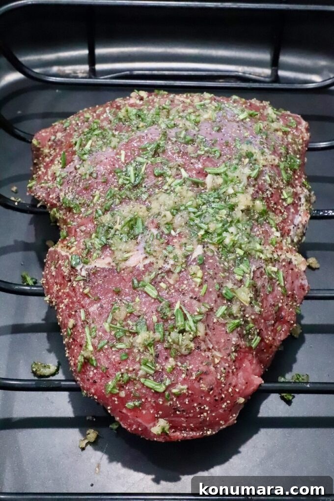 Sirloin Tip Roast Recipe for Tender, Juicy Results 4 Raw seasoned beef roast covered in chopped herbs and spices, resting in a roasting pan.