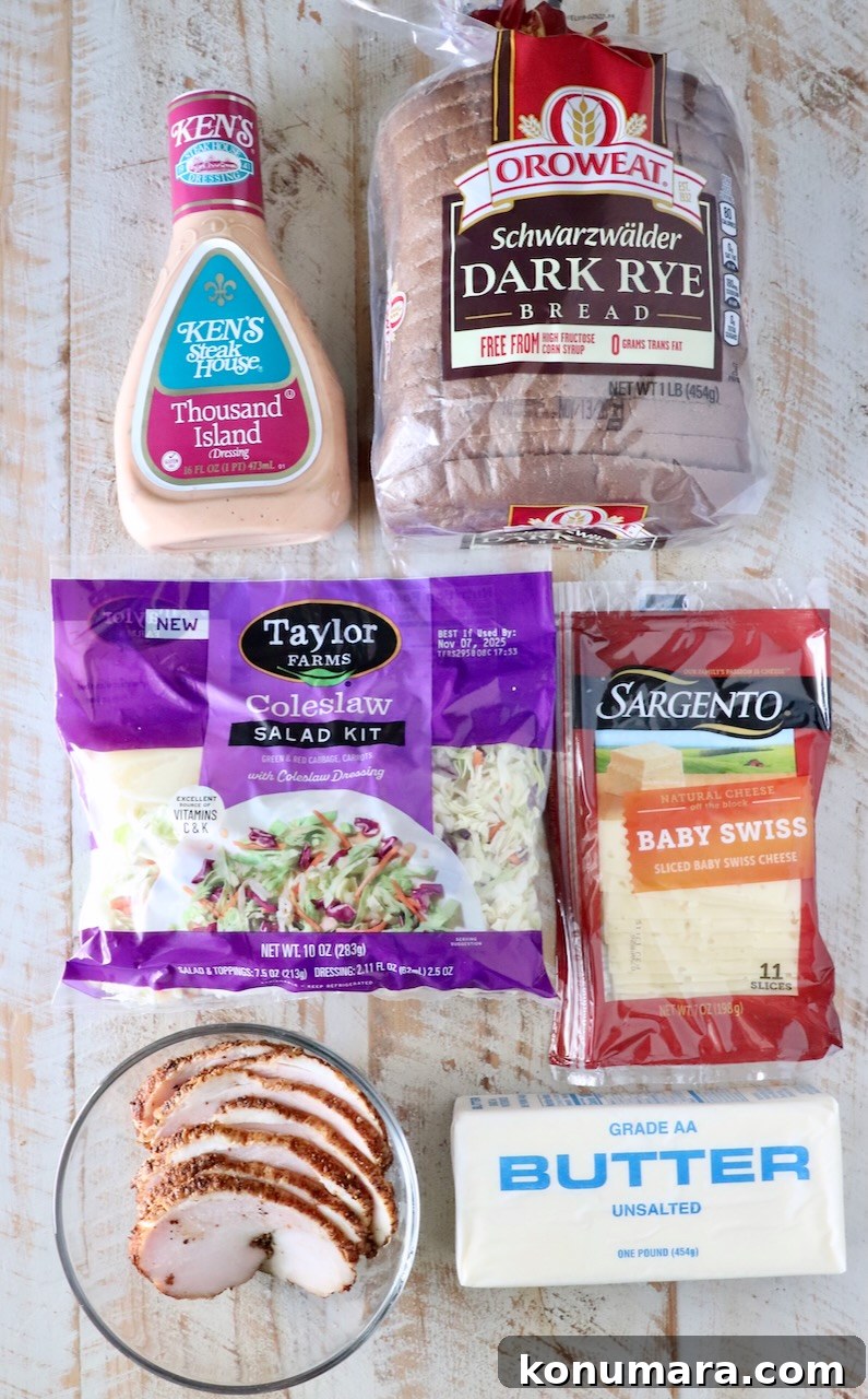 Packaged ingredients on a wooden table include Thousand Island dressing, dark rye bread, coleslaw kit, baby Swiss cheese, sliced cooked turkey, and butter.