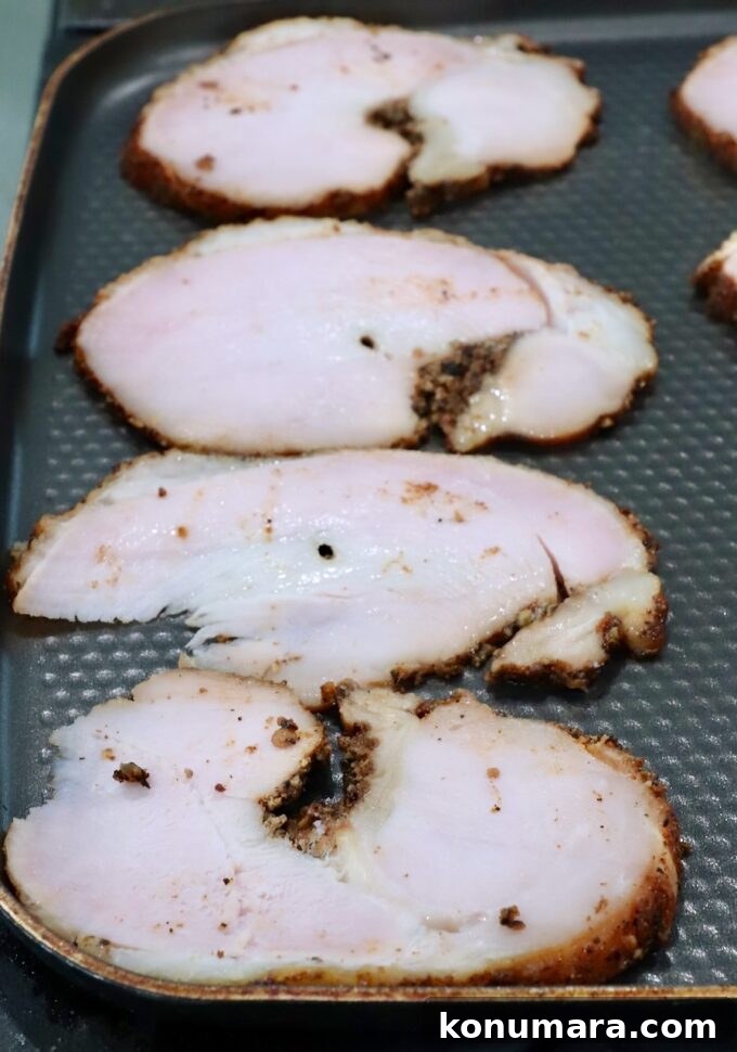 Slices of roasted turkey breast with a browned seasoning crust are laid out on a textured skillet.