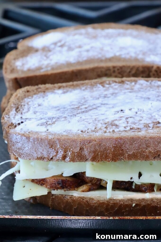 Two sandwiches on a stove. The bread is buttered, with melted cheese and grilled meat peeking out.
