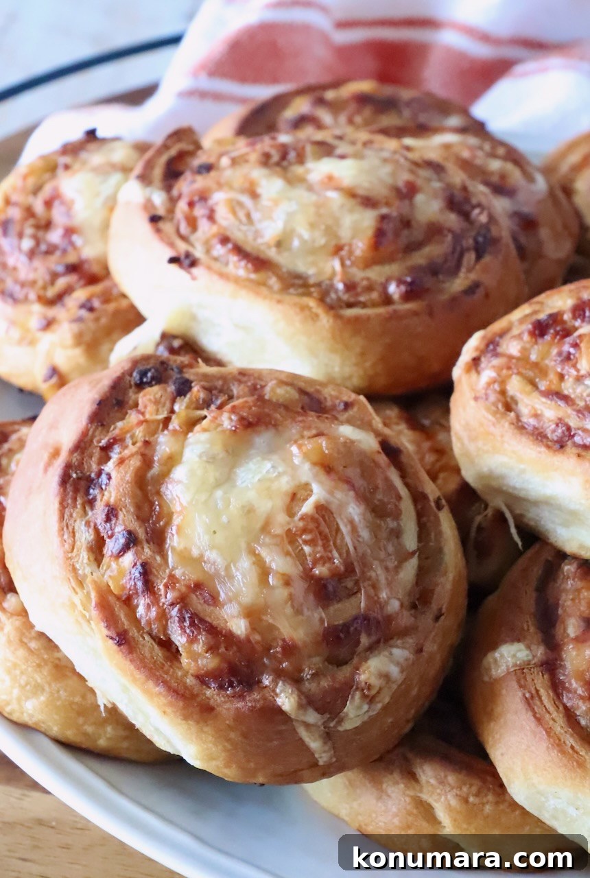 Close-up of golden-brown cheese and onion buns on a white plate. The swirled bread shows a crispy texture.