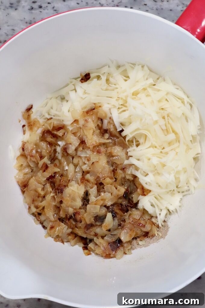 Chopped caramelized onions and shredded cheese in a white mixing bowl on a speckled countertop